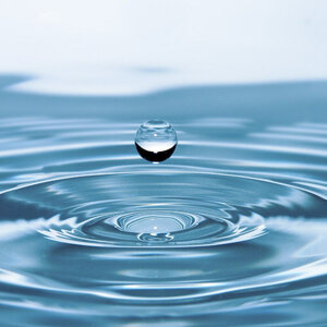 Das Bild zeigt einen Wassertropfen über einer Wasserfläche.